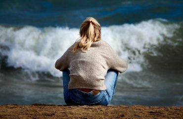 A woman sitting on a beach next to a body of water