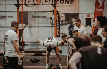 Group of athletes engaging in a competitive CrossFit workout at a gym with emphasis on strength and teamwork.